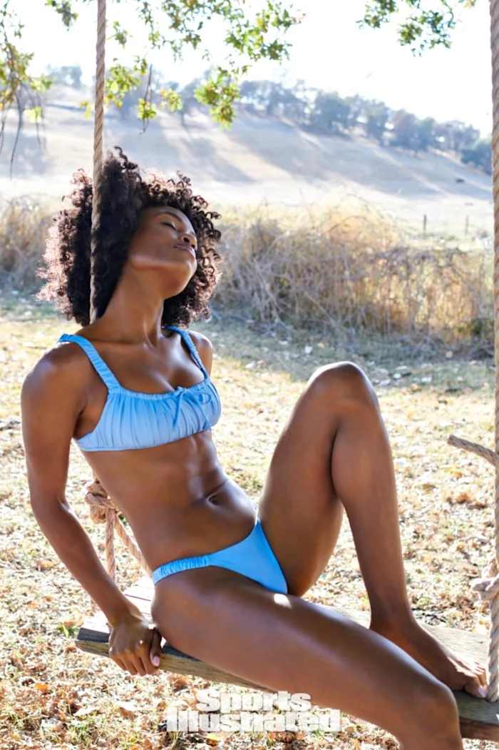 Tanaye White leans back on a wooden swing, wearing a light blue ruched bikini.